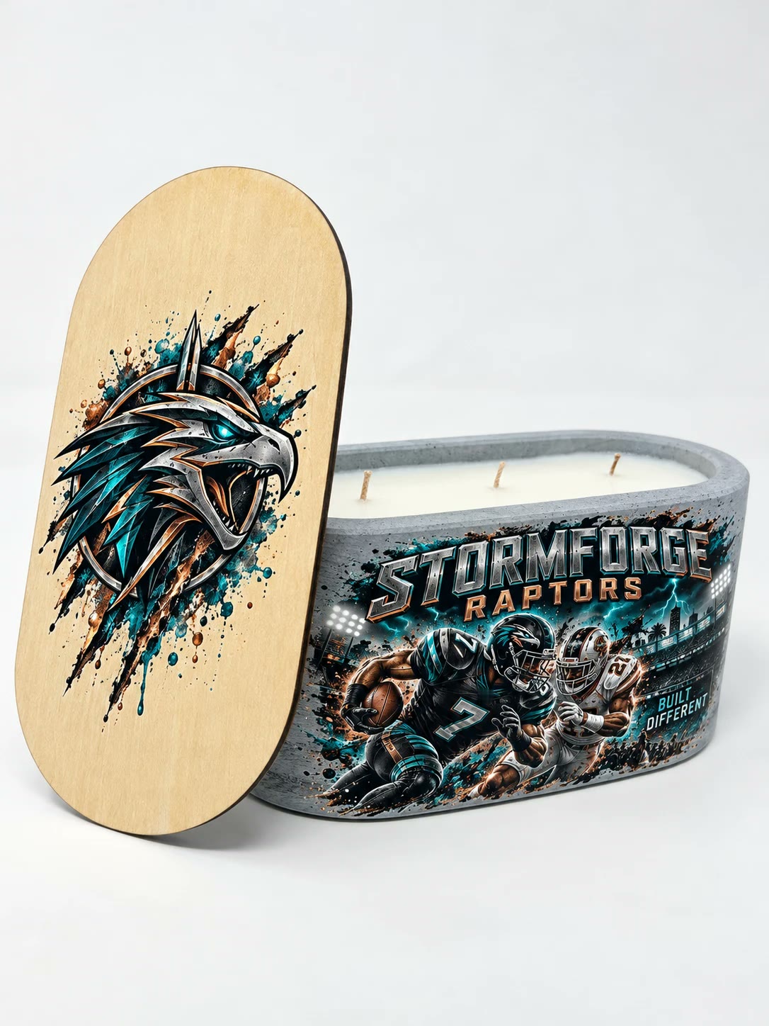 Concrete candle with teal and silver football art reading Stormforge Raptors, its lid with a raptor crest leaning beside it.