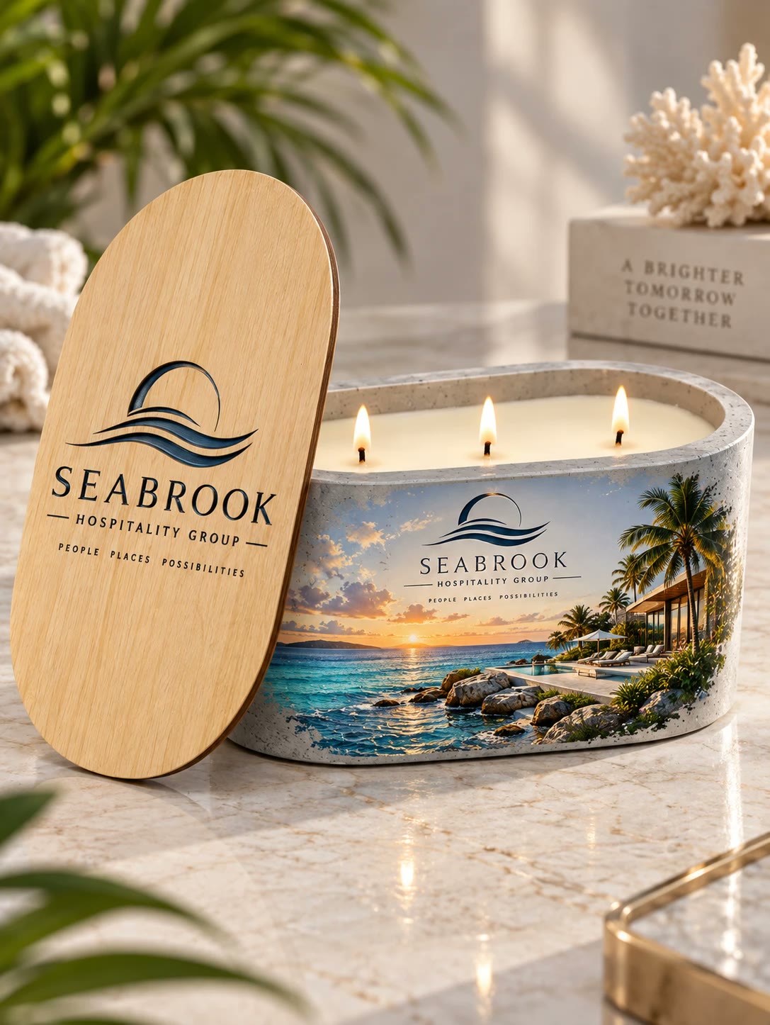 Candle with three lit wicks and a sunset shoreline, the Seabrook Hospitality Group logo on the stone and on the lid leaning beside it.